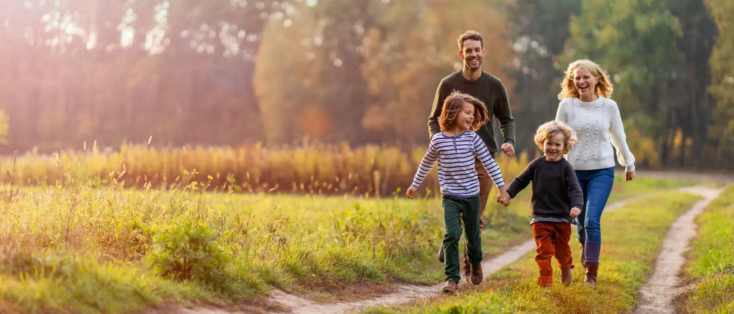 A family of four hikes a trail in a green landscape.